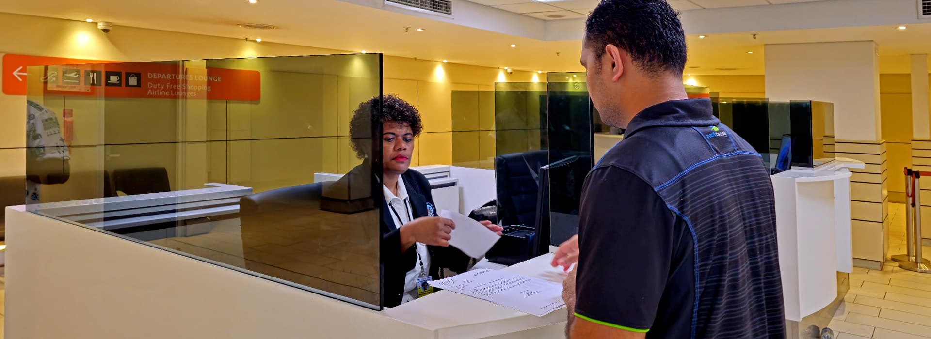 An officer assisting a traveller at an airport departures desk